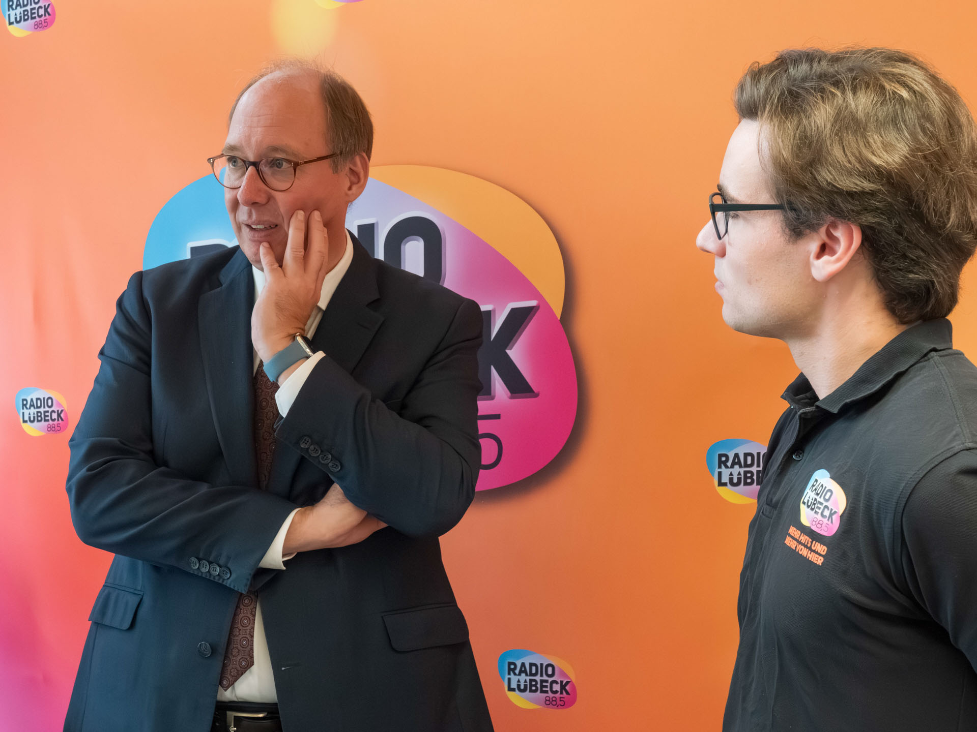 Helge Braun und ein Mitareiter des Radio Lübeck stehen vor einer Wand des Radio Lübeck